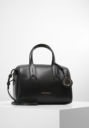 Czarna skórzana torebka Emporio Armani z podwójnymi uchwytami, odpinanym paskiem na ramię i okrągłą markową zawieszką, leżąca na białej powierzchni.