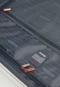 Schwarze Reisetasche mit Mesh-Tasche im Inneren, rose-goldenen Reißverschlüssen und Branding. Enthält Flugzeuggrafiken und Text auf dem Stoff.