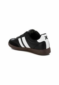 Black leather sneaker with three white stripes, brown rubber sole, and a white heel accent featuring a black cross. Smooth texture overall.