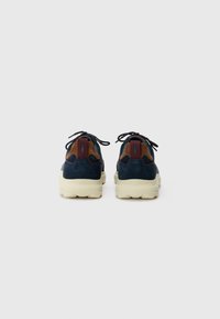 Navy blue suede sneakers with brown accents, cream rubber soles, and black laces. Features padded back and logo detail near the heel.