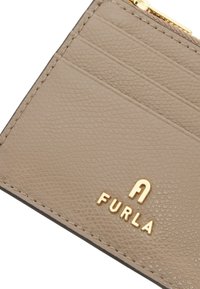 Beżowy skórzany etui na karty z teksturowanym wykończeniem, z złotym logo "FURLA" i wieloma przegródkami na karty z jednej strony. Górna komora zapinana na zamek.