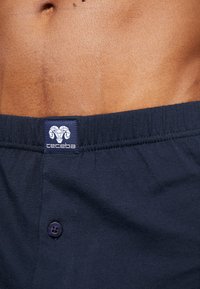 Donker marineblauwe katoenen boxers met een gladde structuur, voorzien van een knoopsluiting en een logopatch met een ramshoop op de tailleband.