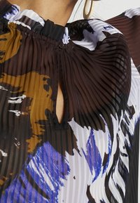 Mehrfarbige Bluse mit horizontalen Streifen in Braun, Schwarz und Weiß, sowie blauen Akzenten; strukturierter Stoff; Knopfverschluss am Hals.