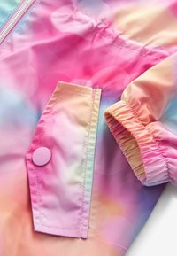 Lekki kurtka w gradientzie pastelowego różu i niebieskiego. Posiada kieszeń zapinaną na zatrzask oraz marszczone mankiety dla dopasowanego kroju.