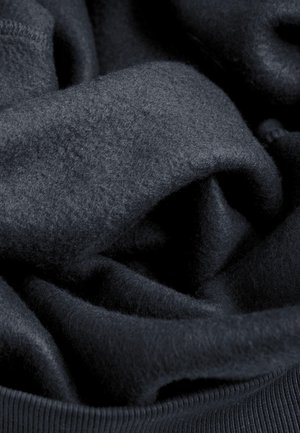 Donkerblauwe gebreide stof met een zachte, pluizige textuur, voorzien van een glad geribbelde zoom. Lagen zijn in een casual opstelling gedrapeerd.