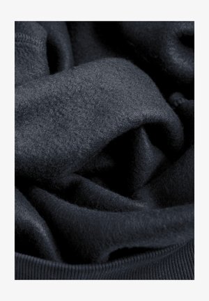 Donkerblauwe gebreide stof met een zachte, pluizige textuur, voorzien van een glad geribbelde zoom. Lagen zijn in een casual opstelling gedrapeerd.