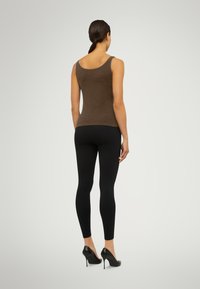 Brun figursydd linne med breda band, kombinerat med svarta leggings och högklackade skor. Slät textur, enkelt design, inga synliga mönster.