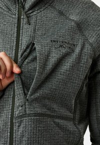 Giacca grigia con zip realizzata in tessuto testurizzato. Presenta un logo in rilievo sul petto e tasche anteriori con zip. Cappuccio foderato e design aderente.