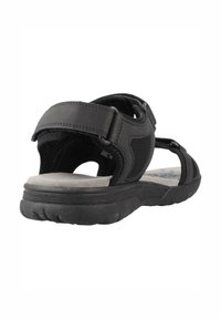 Sandale noire avec un design en maille, une sangle ajustable et une semelle rembourrée. Semelle extérieure en caoutchouc texturé pour une adhérence et une durabilité.