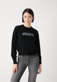 Zwart sweatshirt van zachte stof met een ronde halslijn. Kenmerkt zich door het grijze "HUGO"-logo op de borst. Gecombineerd met donkergrijze jeans.