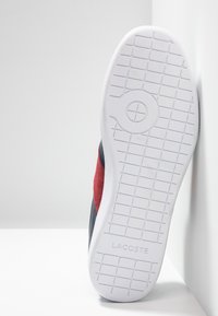 Röd och marinblå mockaskor med en vit gummisula. Texturerat mönster på undersidan och präglad logotyp på sidan.