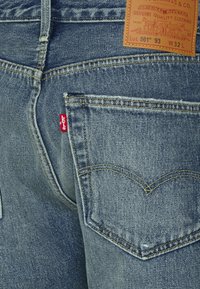 El bolsillo trasero de unos pantalones vaqueros Levi's azules con costuras naranjas, etiqueta roja de Levi's y una etiqueta de marca de cuero marrón que muestra el tamaño W32 L.
