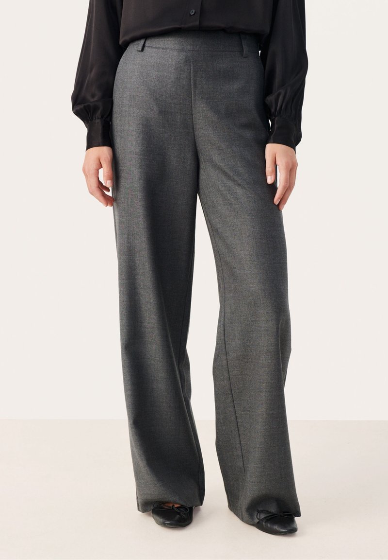 Pantalon habillé gris à jambes larges porté avec un chemisier noir et des ballerines noires sur une personne debout sur un fond uni.