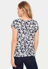 Blusa navy con stampa floreale bianca, maniche corte, tessuto leggero e vestibilità rilassata. Retro mostrato con una morbida texture e scollatura arrotondata.