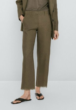 Pantalon vert olive sur mesure avec une légère évasement, doté d'un ourlet effiloché et de poches latérales. Associé à des sandales plates noires.