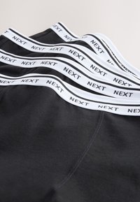 Stapels zwarte boxershorts met witte elastische taillebanden met herhaalde "NEXT" branding.
