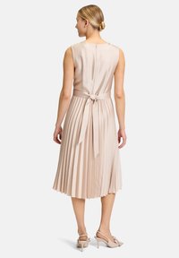 Knielanges, ärmelloses Kleid aus hellbeigem Satin mit einem gefältelten Rock und gebundenem Taillenbereich. Der Rücken hat einen verdeckten Reißverschluss und einen runden Halsausschnitt.