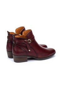 Botas de tobillo de cuero burdeos con punta redonda, tacón bajo y acentos de hebilla en el costado. Textura suave con forro de color marrón claro en contraste.