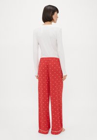 Pantalons de pyjama à motifs rouges avec une taille élastique, associés à un t-shirt à manches longues blanc. Les pantalons présentent un design floral et des accents passepoilés.