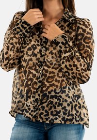 La blusa con stampa leopardata presenta un tessuto trasparente, maniche lunghe, chiusura a bottoni, colletto e una vestibilità comoda. I colori includono beige, marrone e nero.