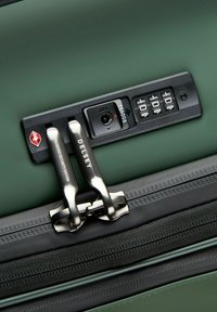 Cadenas à combinaison sur une valise verte avec deux tirettes en métal étiquetées "Delsey" et "Système de sécurité breveté."
