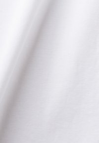 Gros plan d'un tissu blanc uni avec des plis doux et une texture fine visible.