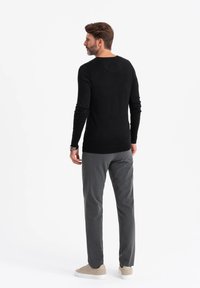 Schwarzer Pullover mit langen Ärmeln und Rundhalsausschnitt, taillierte Passform, kombiniert mit grauen Hosen und beigen Schuhen. Minimale Details, glatte Textur.