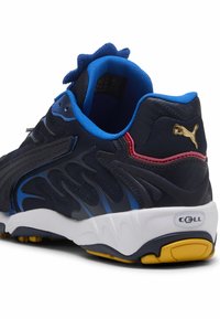 Scarpa sportiva blu navy con fodera blu, accento rosso, suola bianca, battistrada giallo, pattern neri e logo Puma dorato sul tallone.