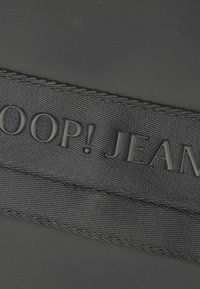 Etichetta in tessuto nero con testo in rilievo "SLOOP! JEANS" in finitura opaca. I bordi cuciti offrono ulteriori texture e durabilità.