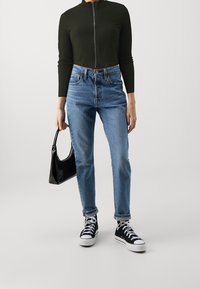 Black ribbed cropped zip-up top, blue high-waisted jeans, black patent handbag, and black high-top sneakers with white soles.
