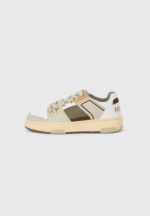 Sneakers with a white, beige, and olive upper featuring mesh panels, orange accents, textured soles, and a prominent logo on the heel.