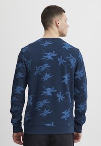 Marineblå sweatshirt med blå blomsterdesign. Har lange ermer, ribbestrikkede mansjetter og rund hals. Myk, teksturert stoff.