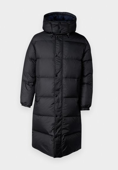 Zwarte pufferjas met een capuchon, voorzien van een gewatteerd ontwerp, drukknopen, elastische boorden en een langere lengte voor extra warmte.