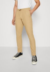 Beige jogger pants with an elastic waistband and drawstring, featuring a slim fit. Paired with black high-top sneakers.