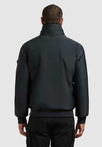 Svart, polstret jakke med høy krage, ribbestrikkede mansjetter og kant. Har en glatt tekstur og minimalistisk design, sett bakfra.