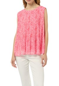 Różowa bluzka z krótkim rękawem z teksturowanym wzorem, luźno opadająca, z okrągłym dekoltem, w połączeniu z kremowymi spodniami.