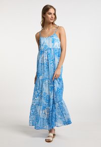 Rochie maxi albastră cu modele florale albe intricate, având bretele ajustabile, o fustă în straturi și un material ușor, vaporizant.
