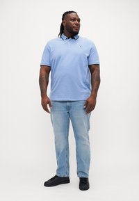Lichtblauwe katoenen polo met een kraag, korte mouwen en een klein logo, gecombineerd met lichtblauwe denim jeans en zwarte sneakers.