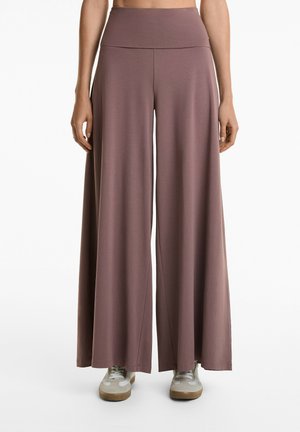 Wide-leg, high-waisted pants in mauve, made of soft fabric. Features a smooth waistband and a flowing silhouette. Shown with light sneakers.