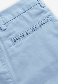 Un tessuto blu chiaro con una superficie liscia presenta un'etichetta cucita con la scritta "BAKER BY TED BAKER" in nero, posizionata su una tasca posteriore.