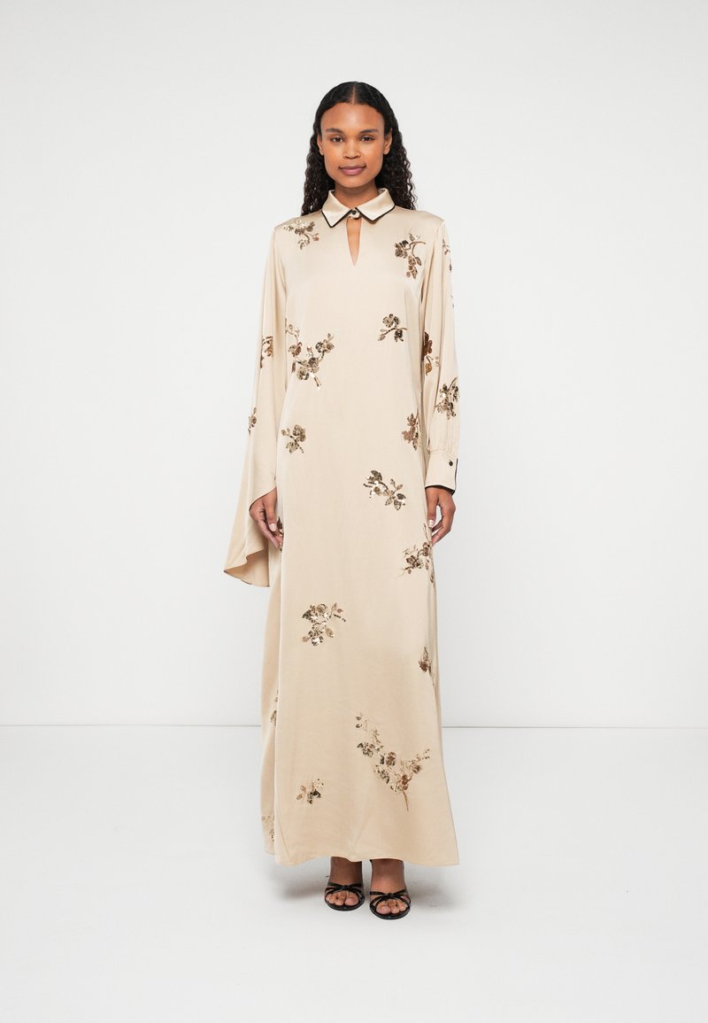 Beige hosszú ruha virágos hímzéssel, kulcslyuk kivágással és kontrasztos gallérral. Hosszú, laza ujjaival és sima textúrájával rendelkezik.