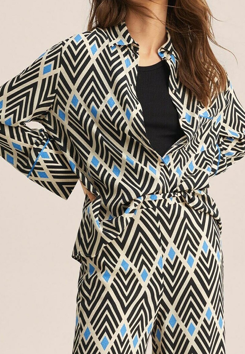 Conjunto de ropa negro y beige con un patrón que presenta diseños geométricos con detalles en azul. Camiseta holgada con cuello y cierre de botones, pantalones a juego.