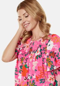 Bluse mit floralem Muster in leuchtendem Pink, mit smockiertem Ausschnitt, kurzen Ärmeln und lockerer Passform. Sie hat große, mehrfarbige Blumendesigns.