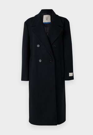 Cappotto in lana nero doppiopetto con colletto a frangia, due tasche frontali e etichetta di marca sulla manica. Tessuto liscio e design su misura.