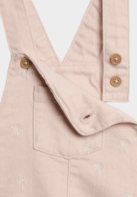 Salopette rosa in cotone con motivi ricamati a forma di palma. Presenta spalline regolabili, bottoni in legno e una tasca frontale.