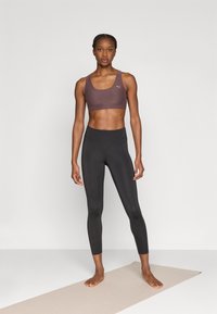 Αθλητικό σουτιέν σε σκουρό καφέ ύφασμα με εφαρμοστή σχεδίαση· μαύρο κολάν από απαλό, ελαστικό υλικό· και τα δύο κατάλληλα για αθλητικές δραστηριότητες.