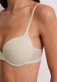 Reggiseno a coppa modellata beige con pannelli laterali in pizzo e spalline regolabili con il marchio "Marc O'Polo" su un torso superiore femminile.