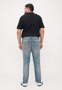 Fekete polo ing, világoskék denim farmer, egyenes kivágás, öt zsebes kialakítás és fehér sznekkerek fekete csíkokkal.