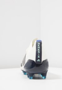 Botas de fútbol blancas con rayas negras, con una parte superior texturizada, talón con acento azul y tacos azules para mayor tracción.