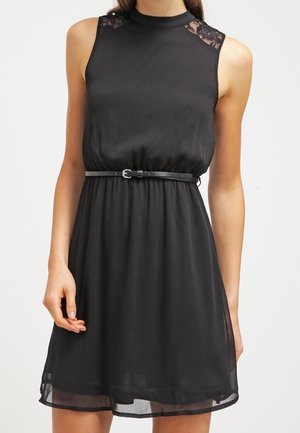 Vestido negro sin mangas con cuello alto, detalles de encaje en los hombros, cintura ceñida con un cinturón negro delgado y dobladillo transparente.